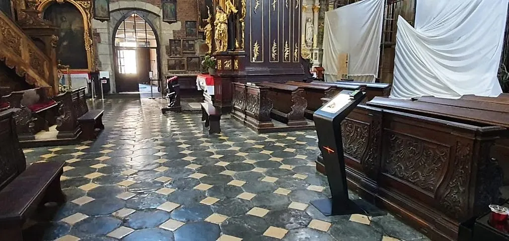 Spendenautomat an der Bankreihe einer Barockkirche, im Hintergrund das offene Portal.