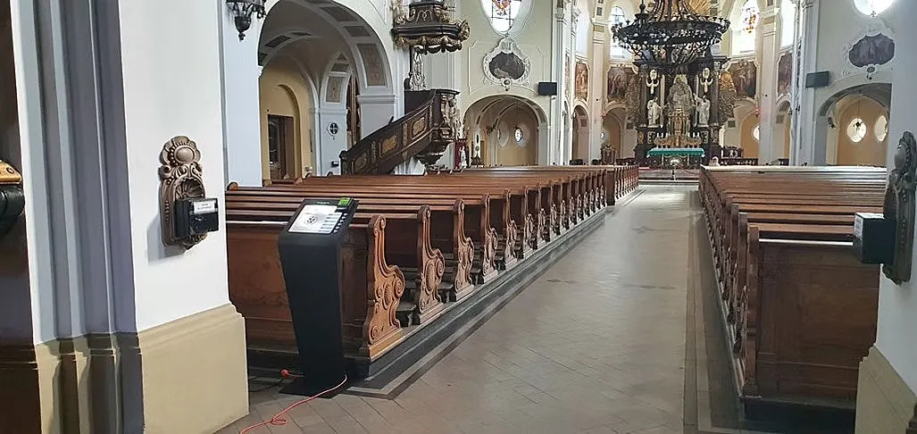 Spendenautomat am Mittelgang einer hellen Barockkirche, Blick zum Hochaltar.