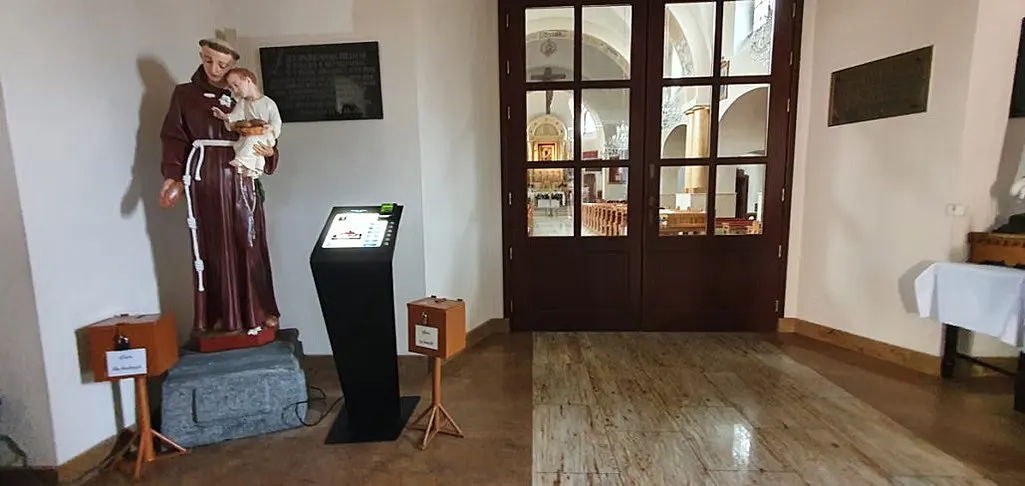 Spendenautomat im Eingangsbereich zwischen einer Heiligenfigur und zwei hölzernen Opferstöcken.